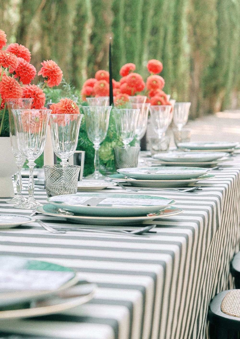 Long banquet table dressed in striped Appolonia linen with red dahlias